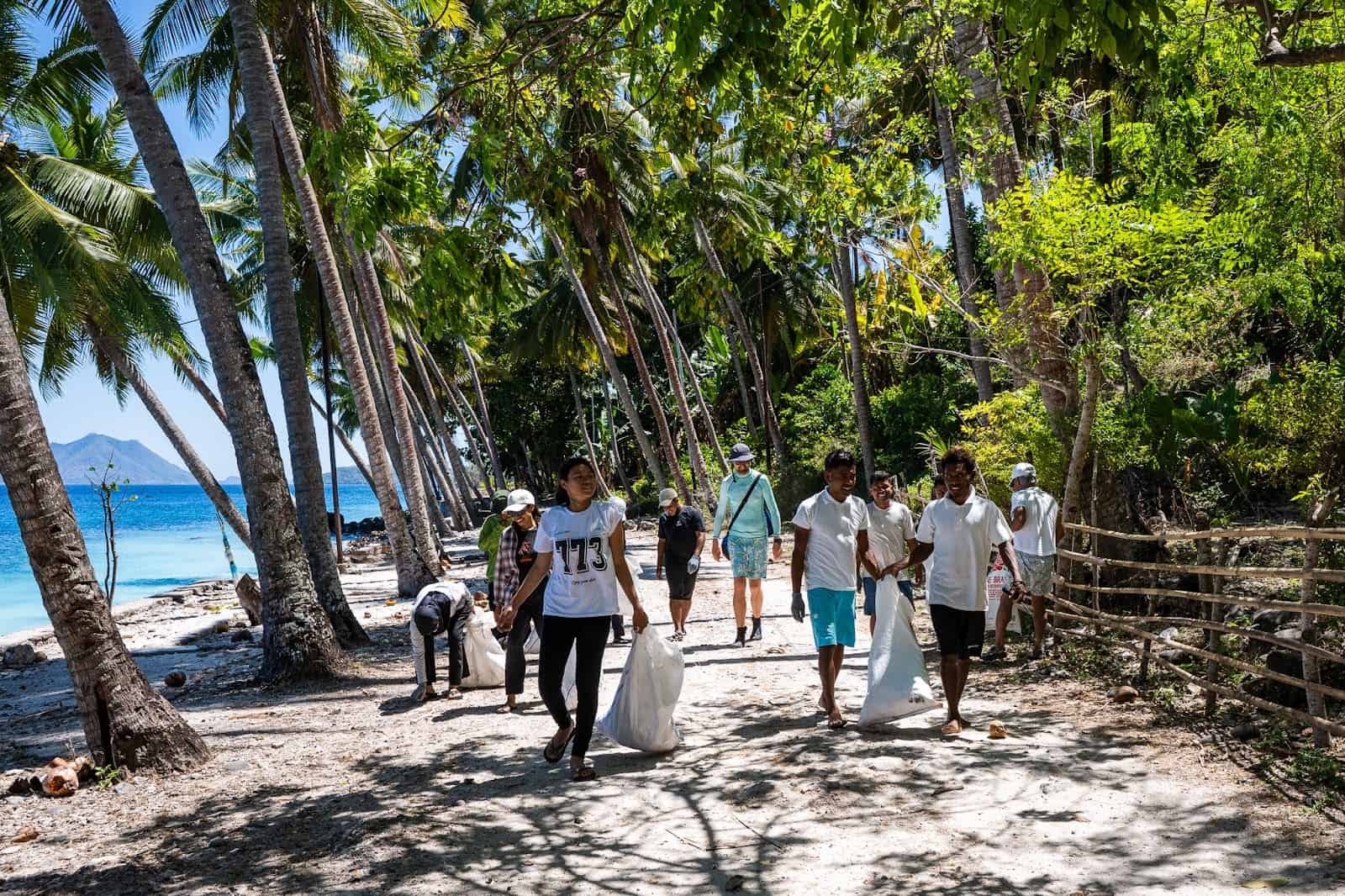 Travelers walking along a shaded beach path, carrying trash bags and picking up litter.