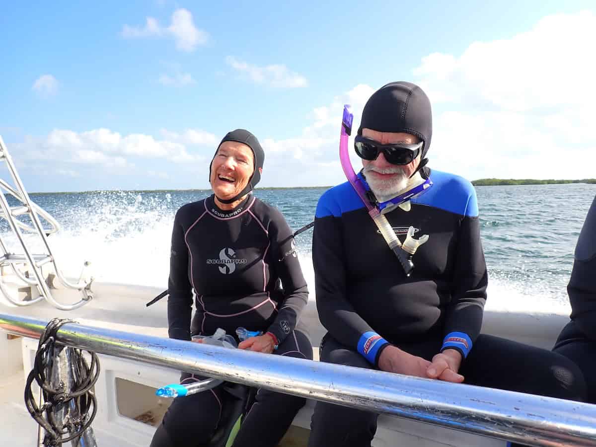 Two snorkelers in wetsuits standing on a boat, ready for a snorkeling adventure in Jardines de la Reina, Cuba.
